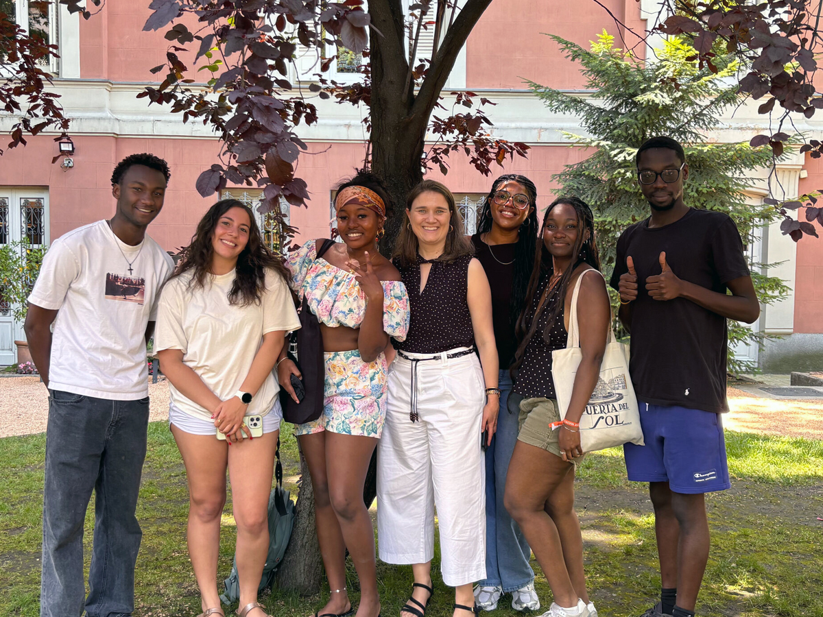 Students pose with a program leader under a tree outside a pink building in Madrid.