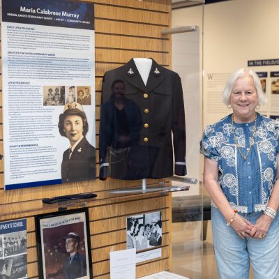 Woman standing beside museum exhibit honoring WAVES officer Maria Calabrese Murray