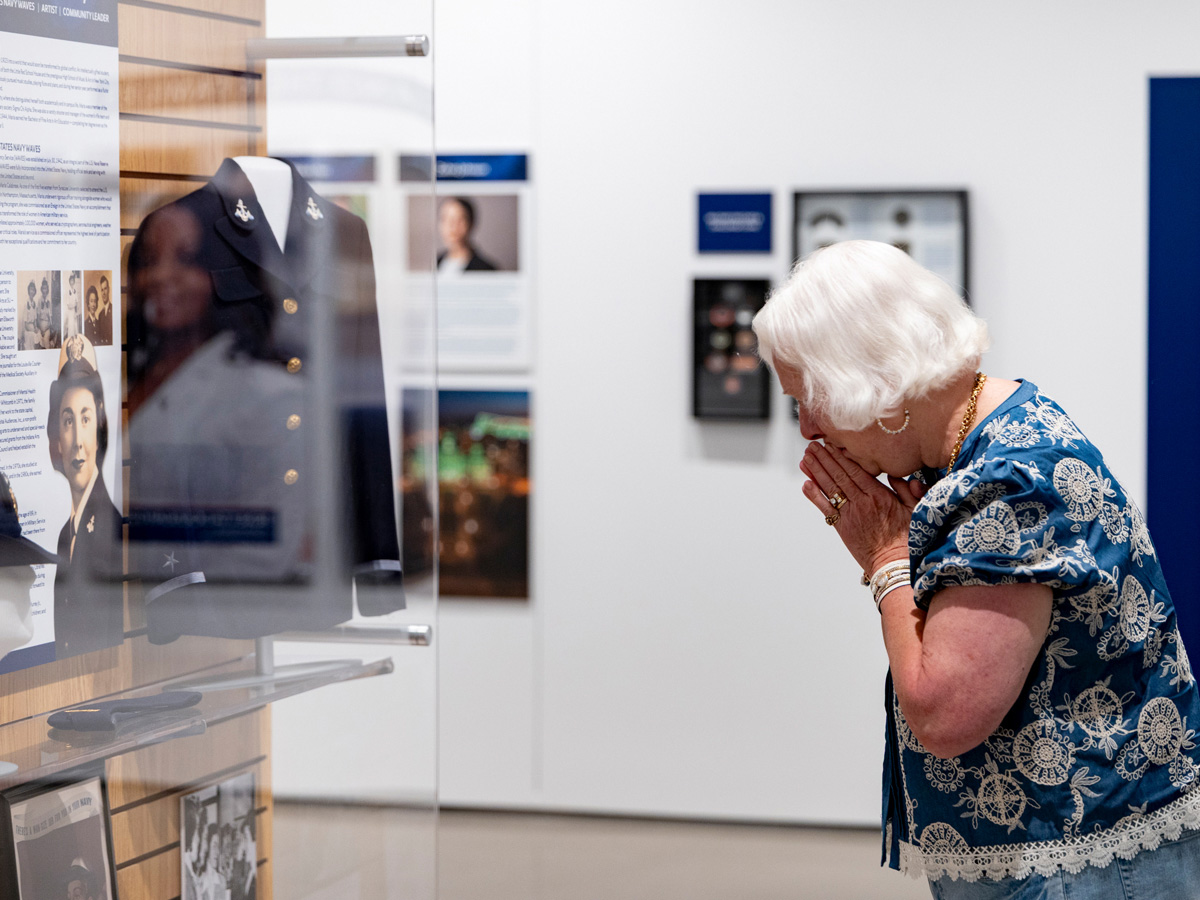 Woman emotionally viewing museum display of Maria Calabrese Murray's Navy uniform