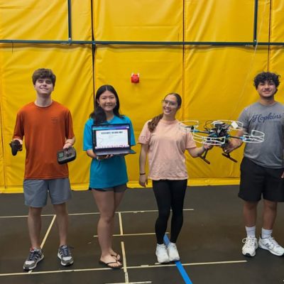 Students hold a drone, laptops and controllers in Orange Works.
