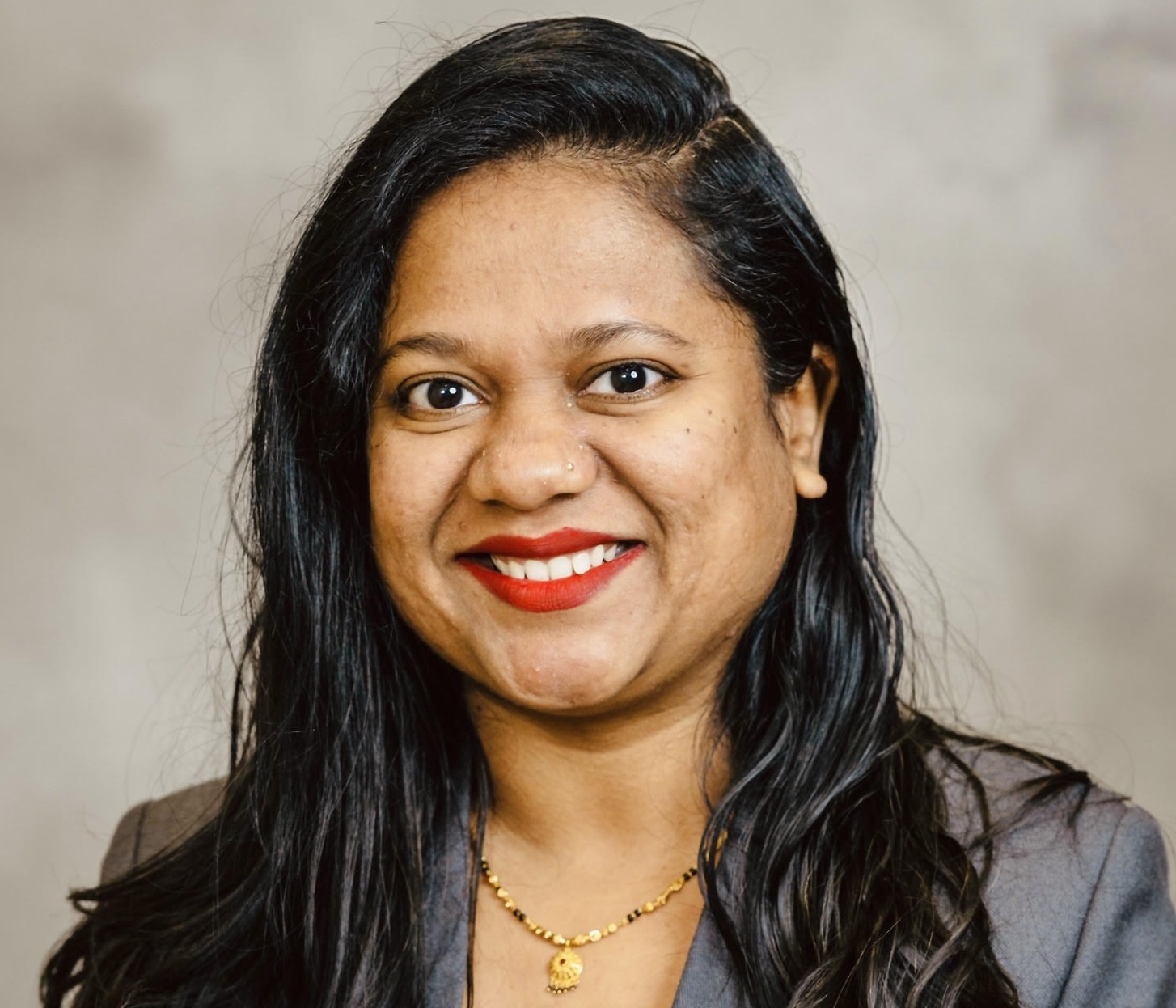Professional headshot of a person in a gray blazer against a neutral background.