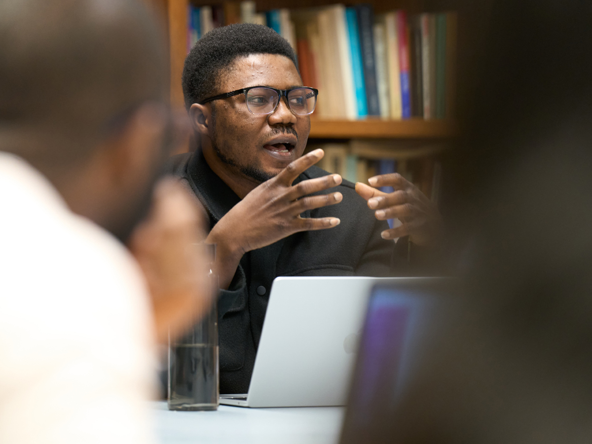Ebenezer Makinde gestures while speaking, seated before a bookshelf