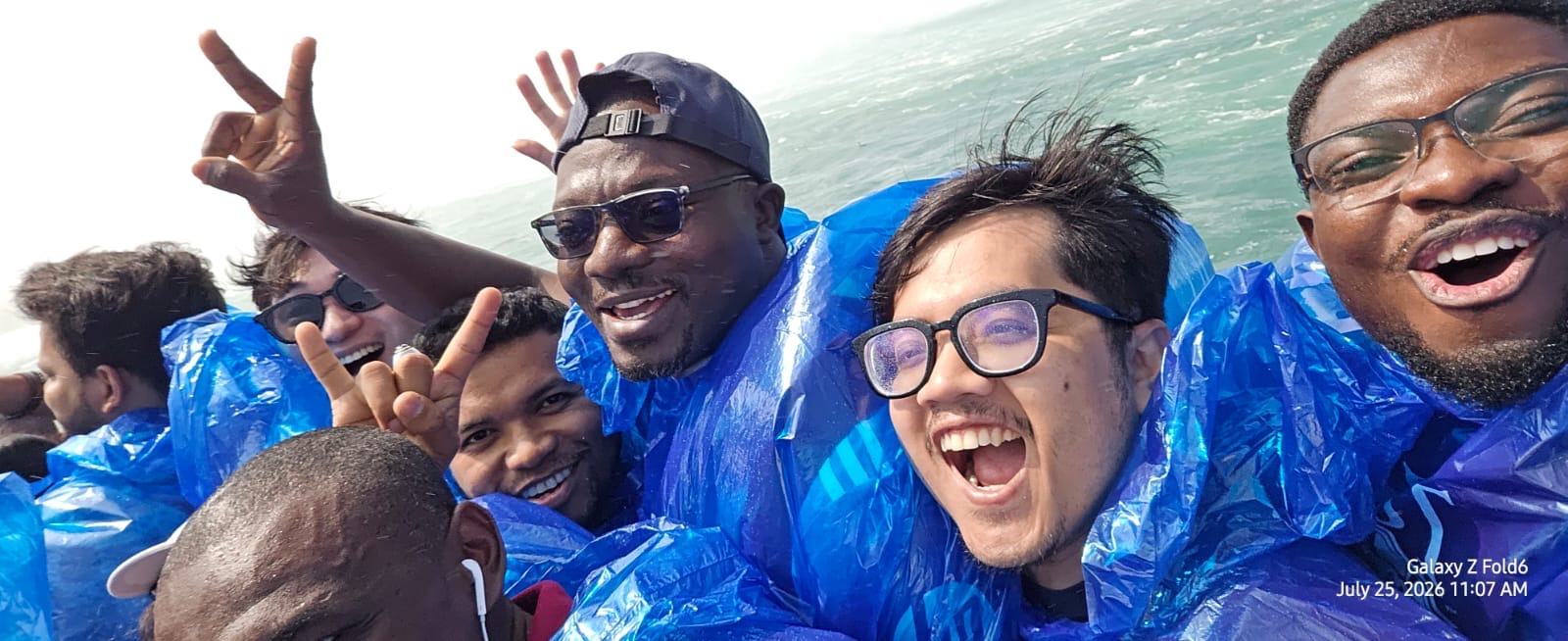 Group of people in blue rain ponchos taking a selfie on a boat near Niagara Falls.