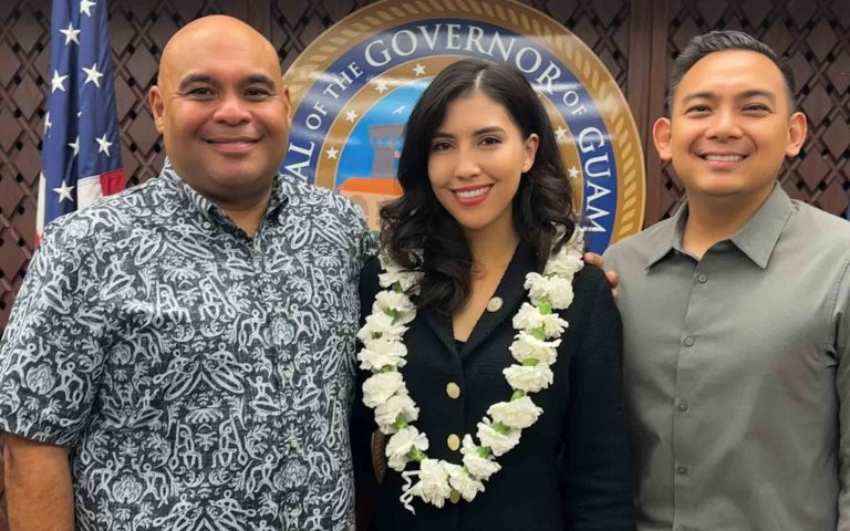 Sarah Elmore-Hernandez with two men in front of the Governor of Guam seal
