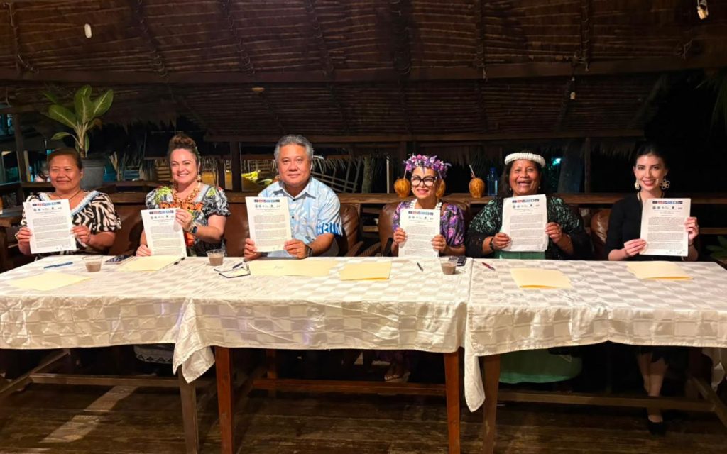 Six people at a table holding up signed documents,