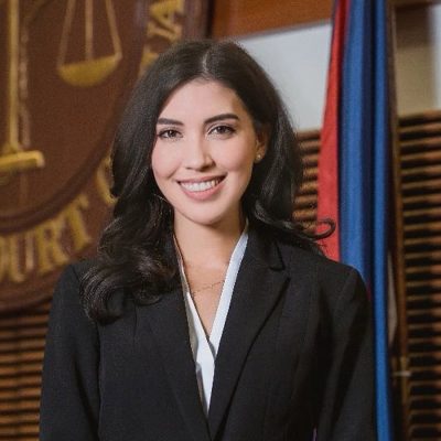 A person smiling in a courtroom near the Guam flag