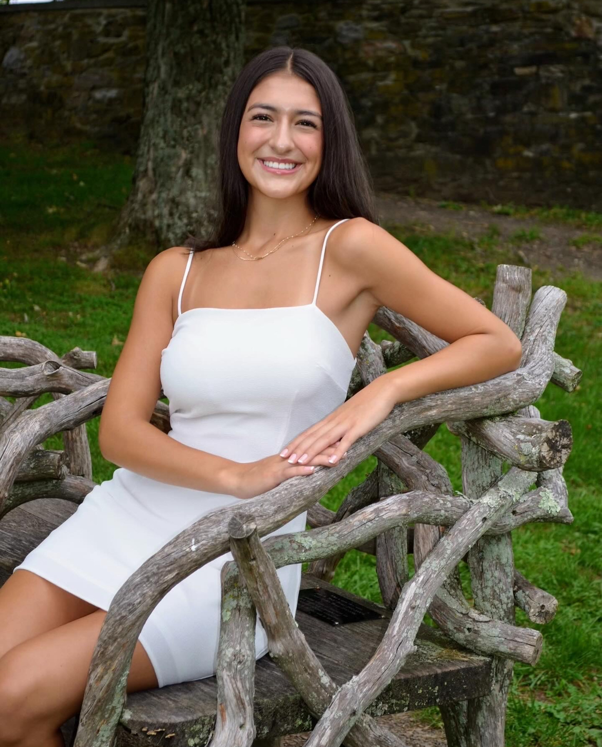 Person seated on a rustic wooden bench outdoors, wearing a light-colored dress.