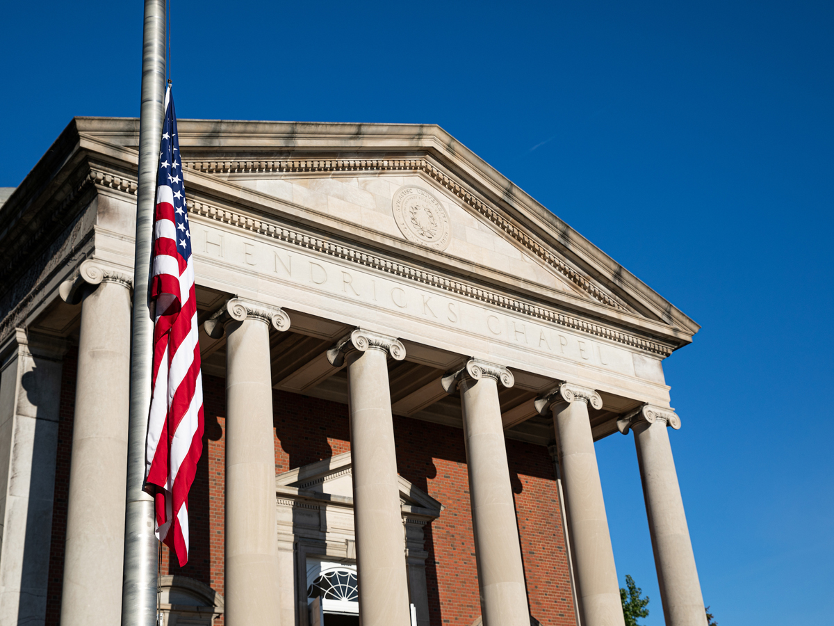 Hendricks Chapel's columned facade with American flag at half-staff against blue sky.