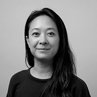 Black-and-white headshot of a woman with long dark hair, smiling slightly, wearing a dark top against a plain gray background.
