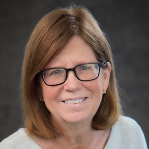 A person smiles while posing for a headshot while seated indoors.