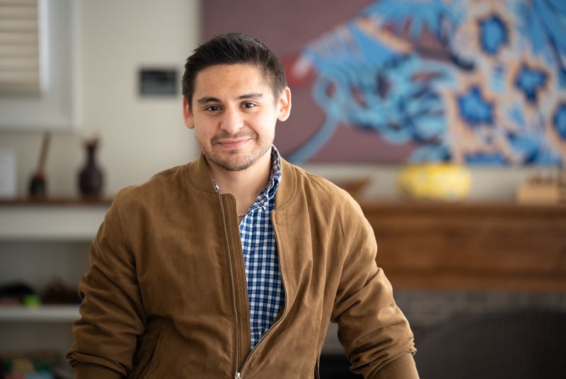 A young man smiles while sitting in a living room.