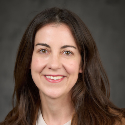 A person smiles while posing for a headshot in front of a dark backdrop.