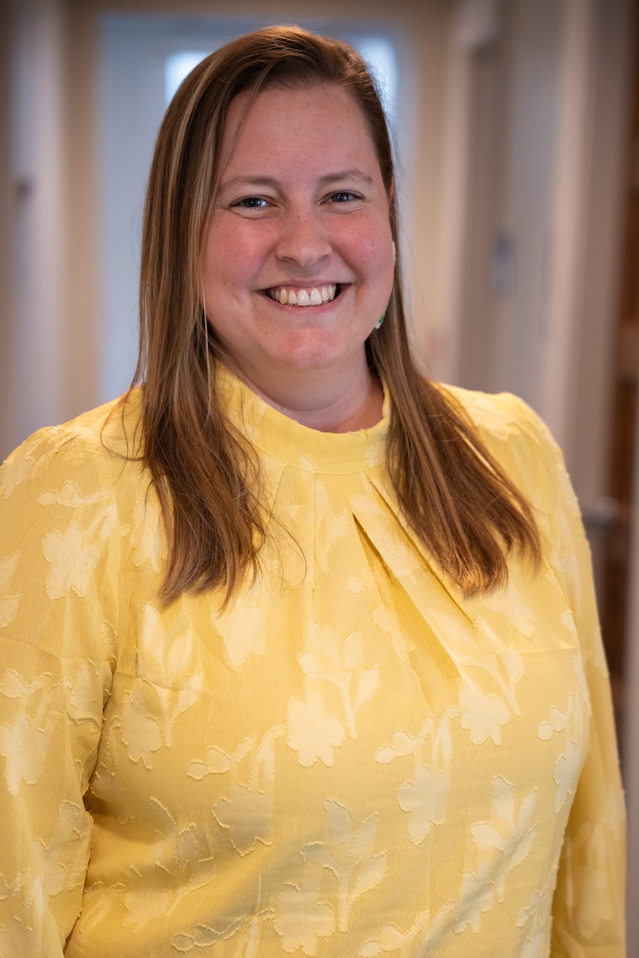 Person in a yellow blouse standing indoors for a portrait.