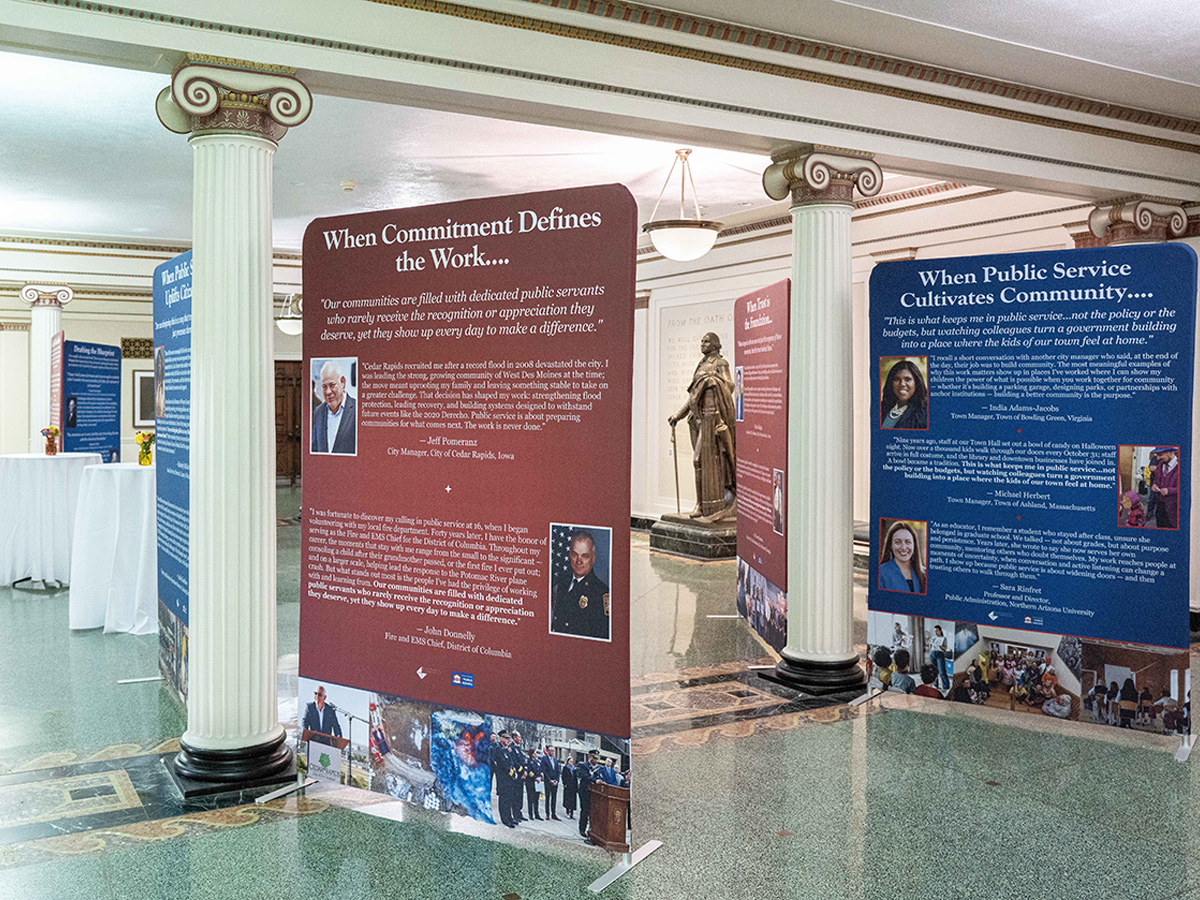 Freestanding exhibit panels featuring public servants' photos and quotes stand in a columned lobby.