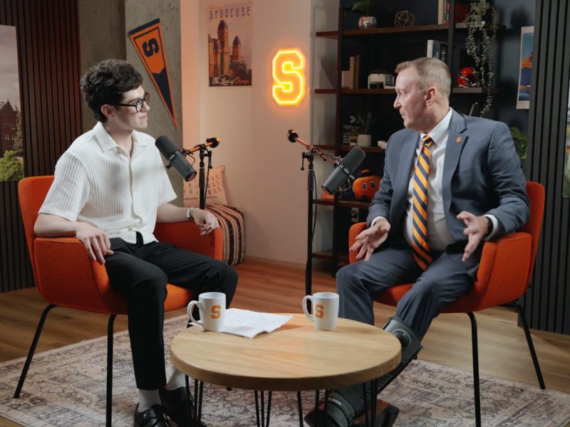 Chancellor Haynie speaks with staff member in a podcast studio decorated with Syracuse memorabilia.