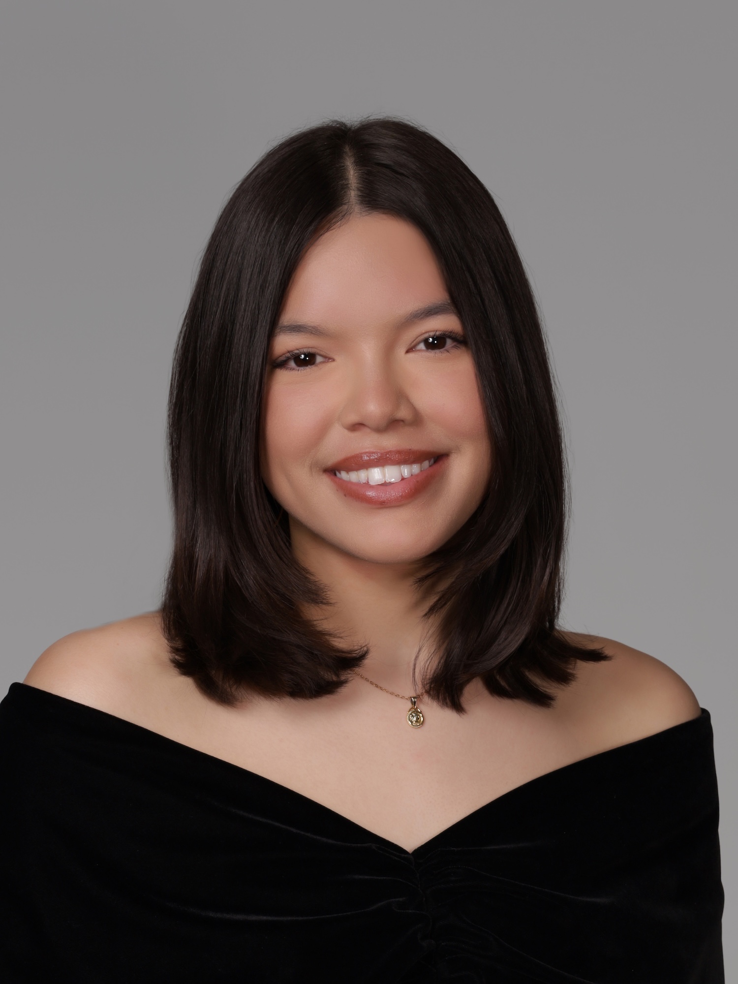 Professional headshot of a person with shoulder-length dark hair against a gray background.