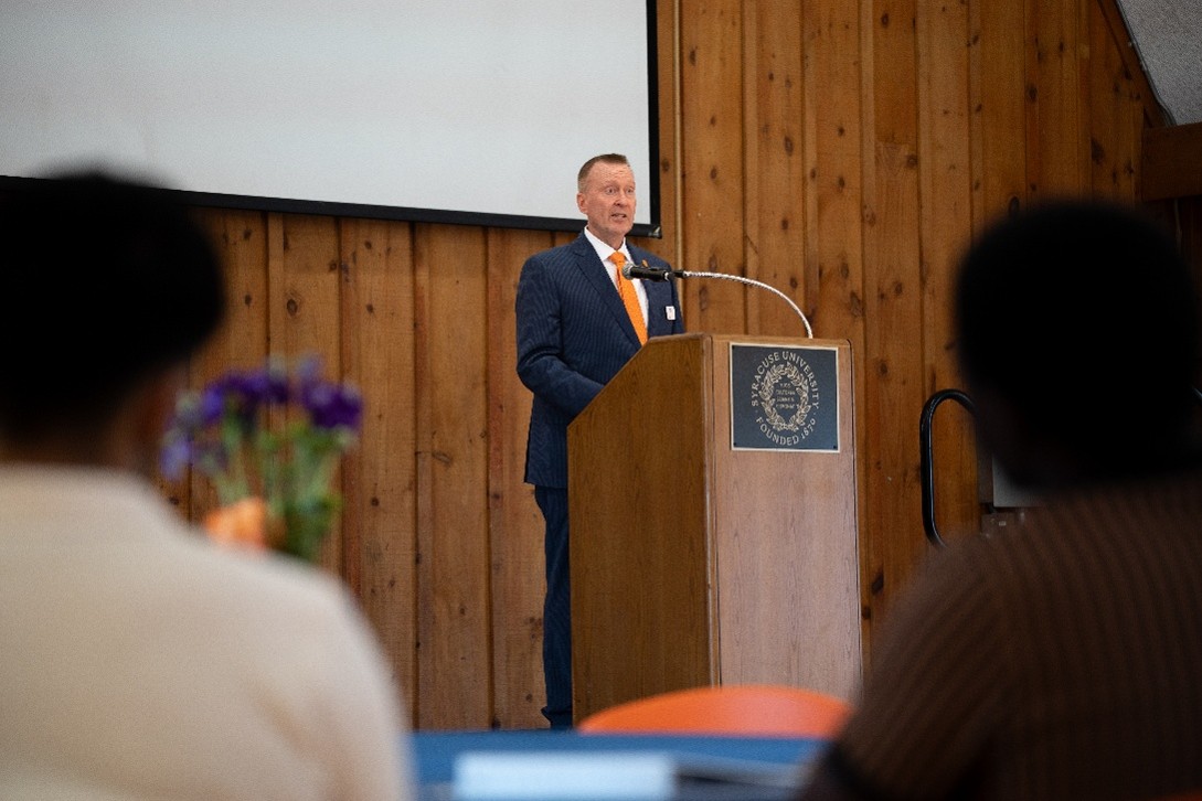A speaker addresses an audience from a podium at a Syracuse University event.