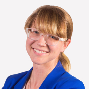 A person in glasses wearing a blue blazer poses for a headshot.