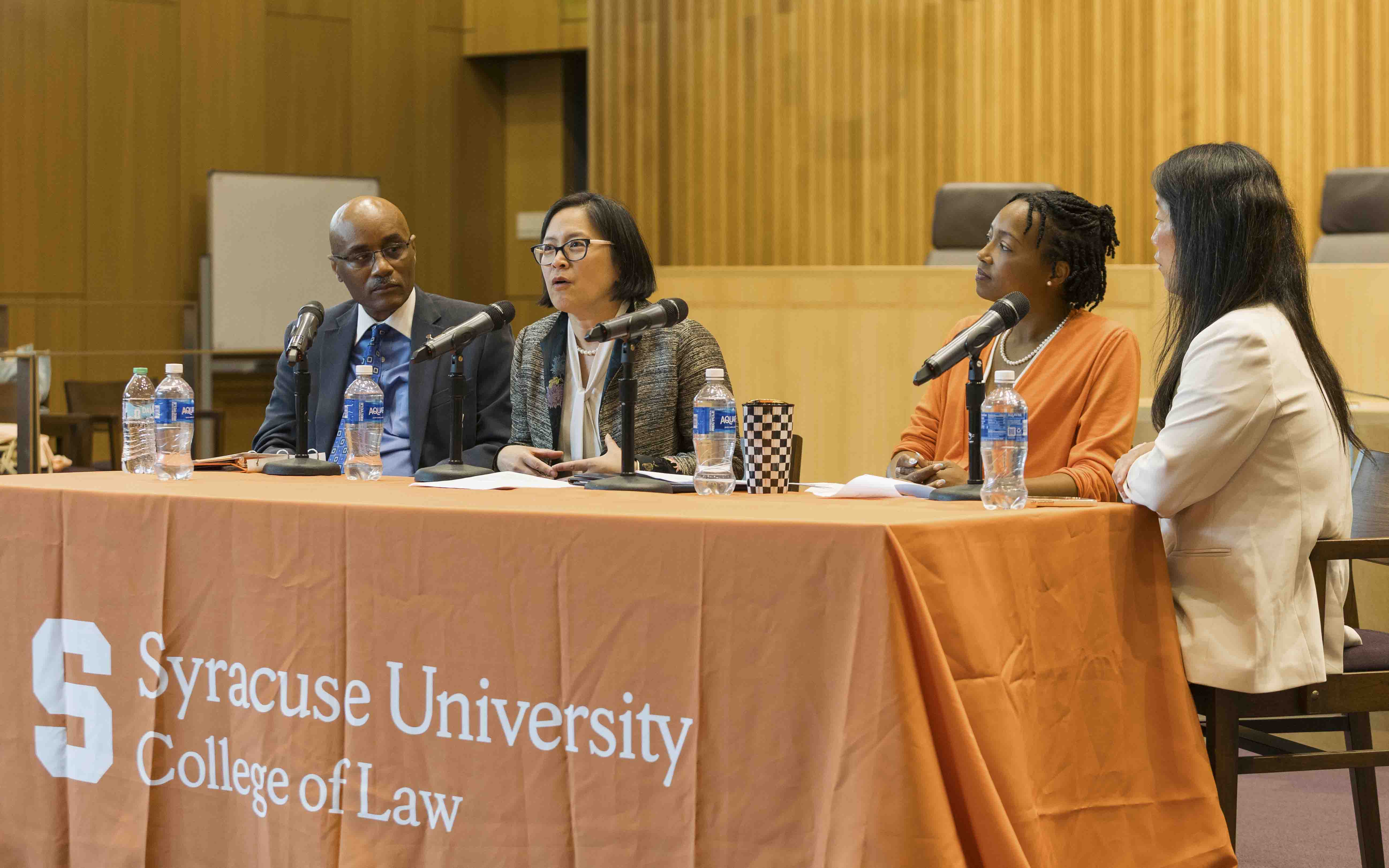 Four panelists seated at a table with an orange Syracuse University College of Law tablecloth, speaking into microphones