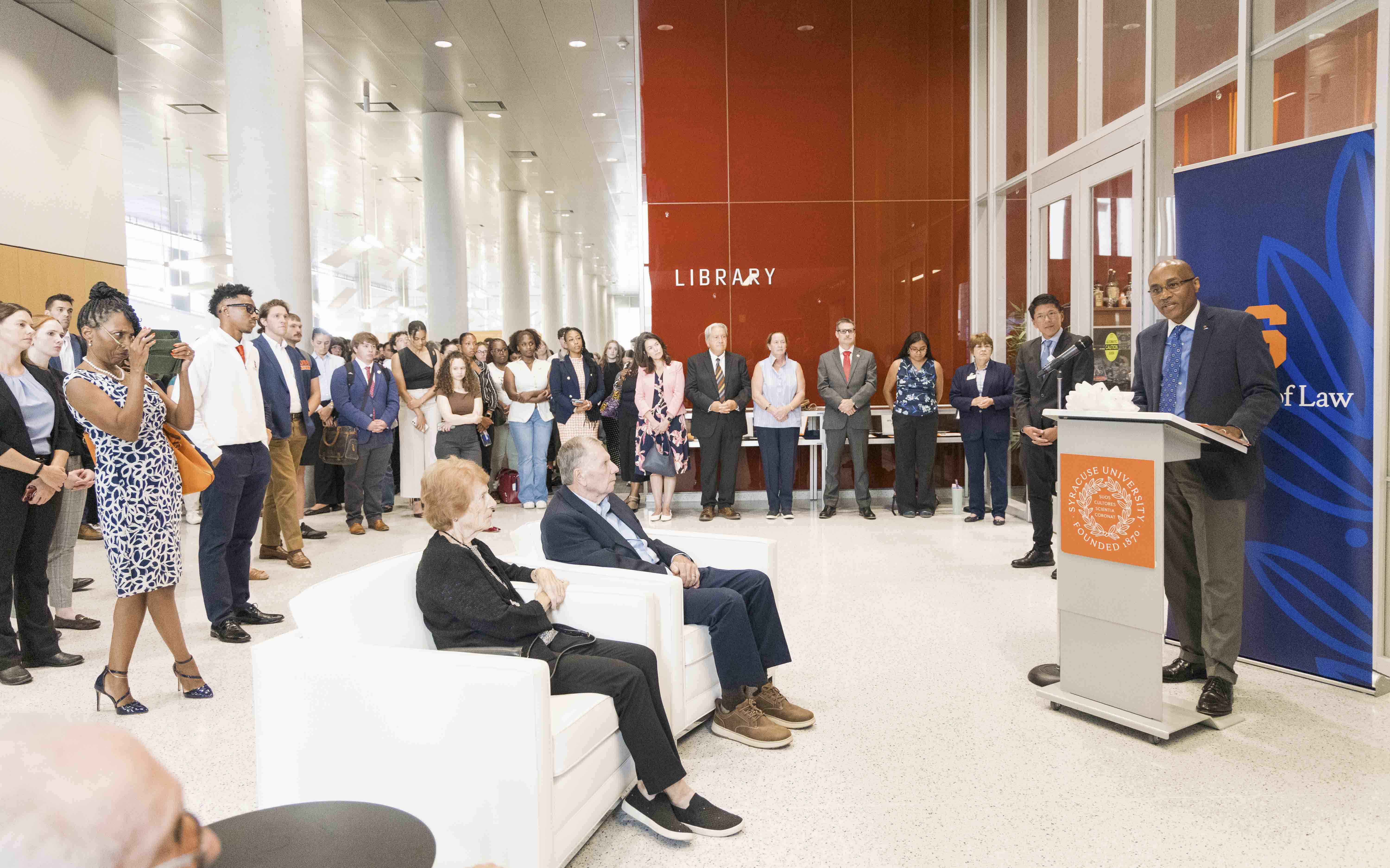 a person at a podium speaks to a group of people sitting and standing