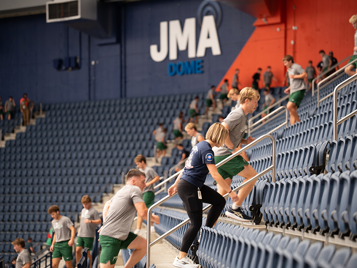 Athletes in workout gear run stair sprints up the stadium seating at JMA Wireless Dome