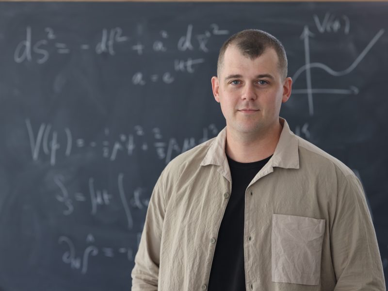 Person standing in front of a chalkboard covered with mathematical equations and graphs in a classroom setting.