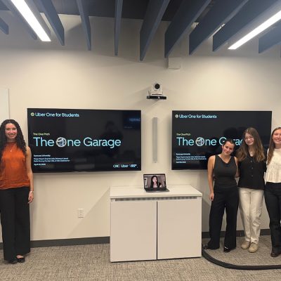 Students present The One Garage pitch during a classroom session, with presentation screens displayed behind them.