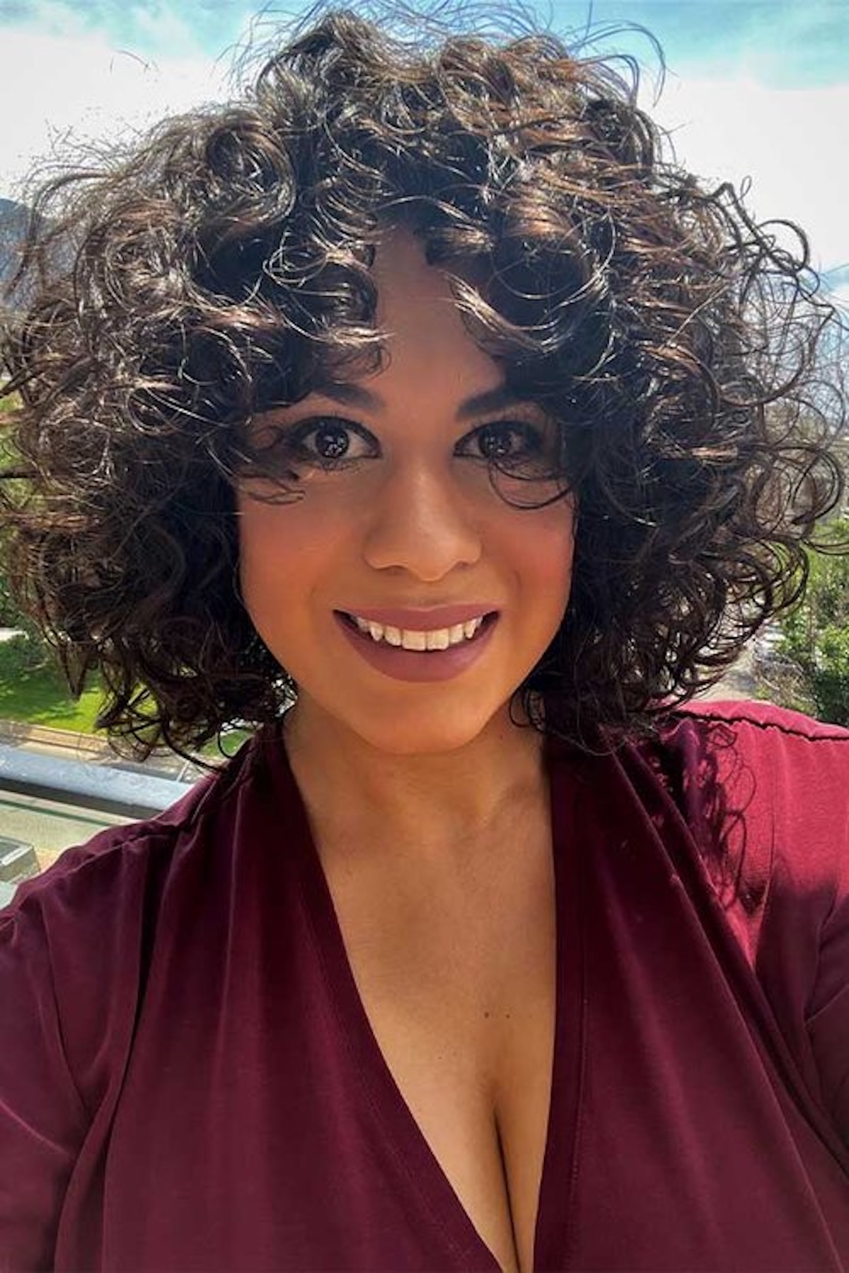 Portrait of Catherine García outdoors, wearing a burgundy top, with short curly dark hair and a direct gaze toward the camera.