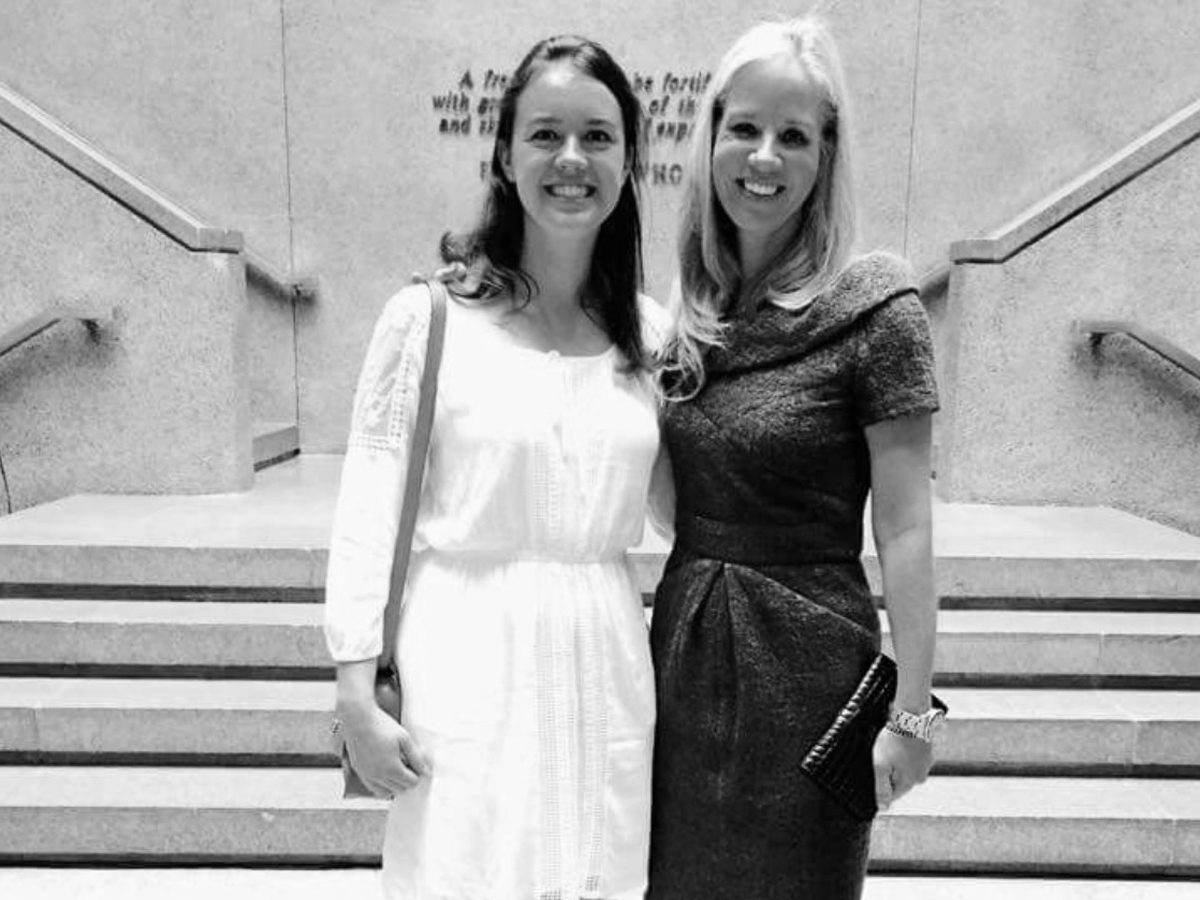Two smiling women pose together on a stone staircase in a black-and-white photo.