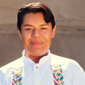 A student smiles in a white shirt with colorful floral embroidery.