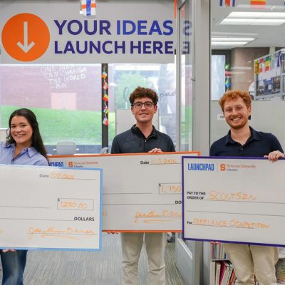 Three student entrepreneurs pose with their winning checks.