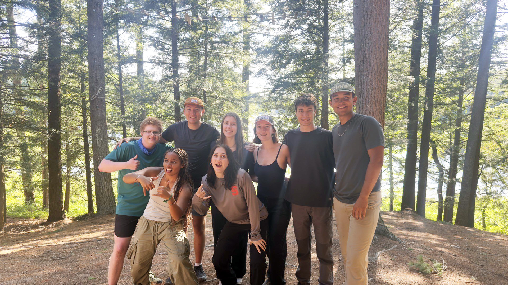 Nine students pose and smile on a hike in a sunny pine forest