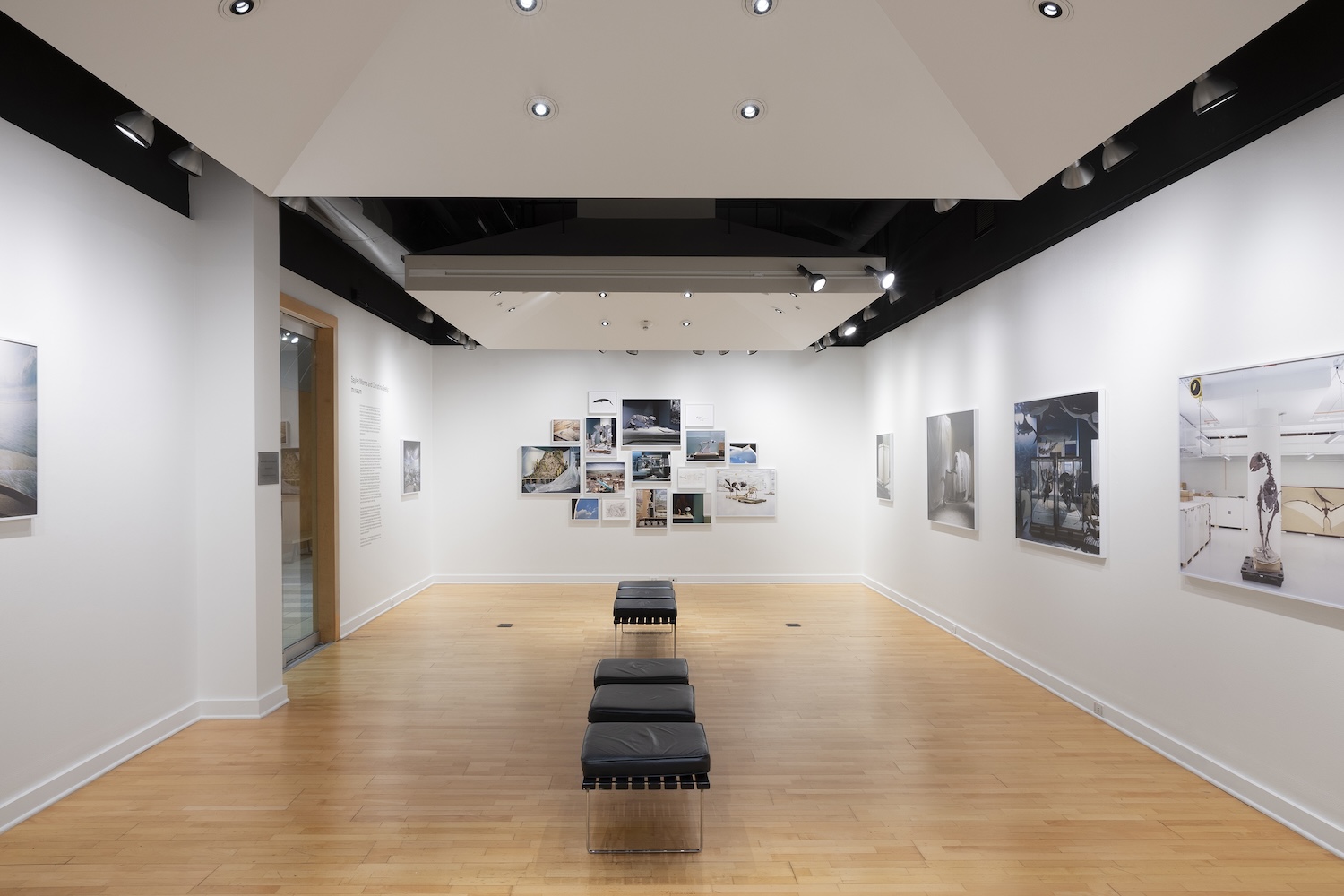 Wide view of a gallery exhibition featuring framed photographs on white walls and benches centered in the room.