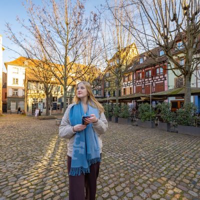 Student standing in a cobblestone square lined with colorful half-timbered buildings in Strasbourg.