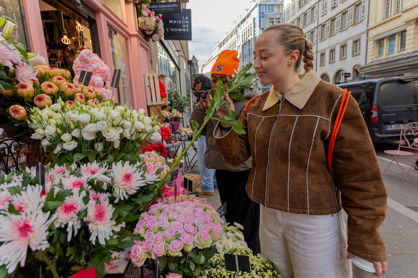 Person smelling a flower while browsing a colorful outdoor flower market.