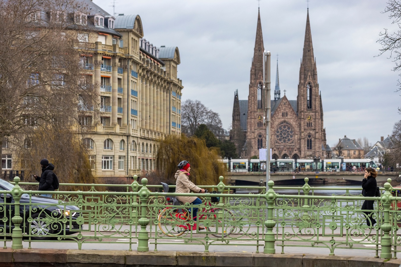 Cyclist crosses a bridge in Strasbourg with a cathedral and historic buildings in the background.