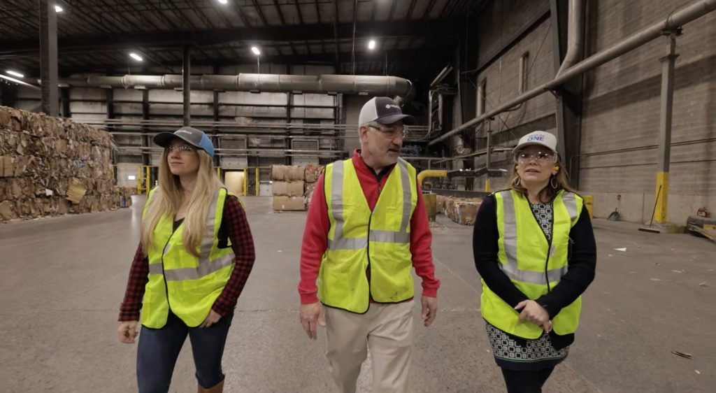 Three people in reflective safety vests walk through a recycling facility.