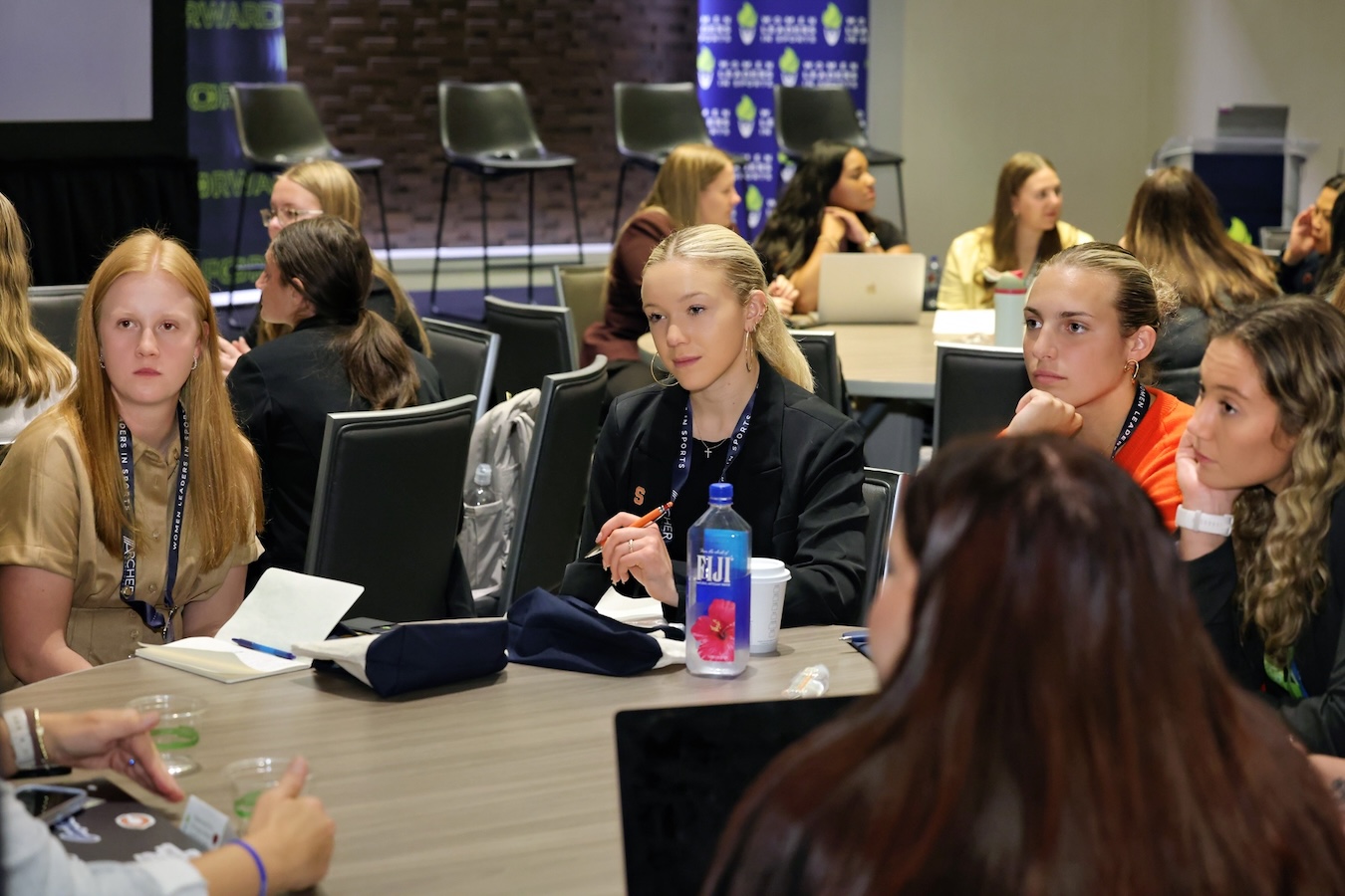 Small-group discussion at a leadership conference, with participants seated around a table taking notes.