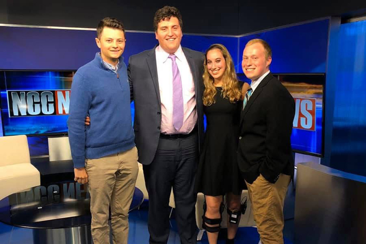 Four students pose in a TV news studio set