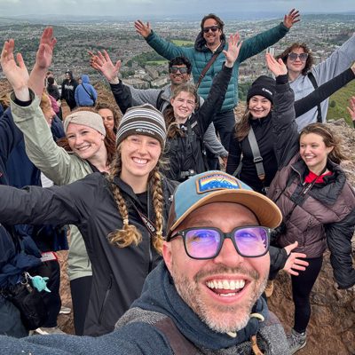 Students and a professor smile for a group photo with their arms extended.