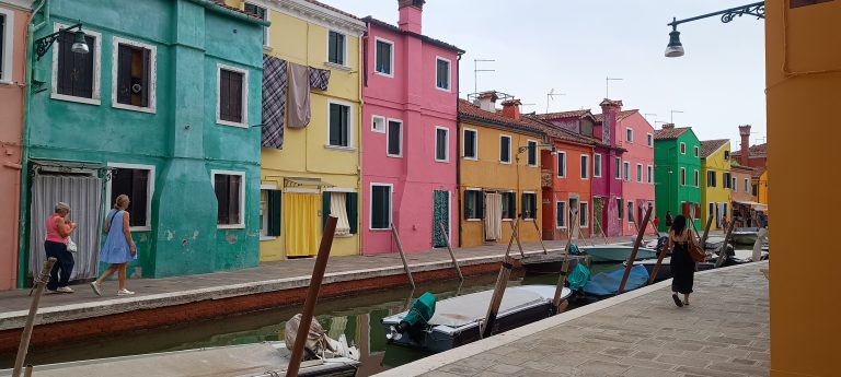Brightly colored houses lining a narrow canal with moored boats along the waterfront.