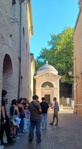 Group of people walking through a narrow brick-lined street toward a small domed historic building.