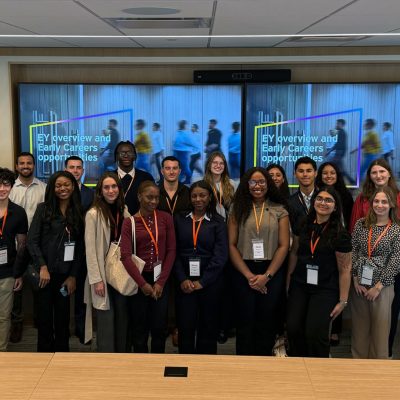 Students in lanyards pose in a conference room before screens reading “EY overview and Early Careers.”