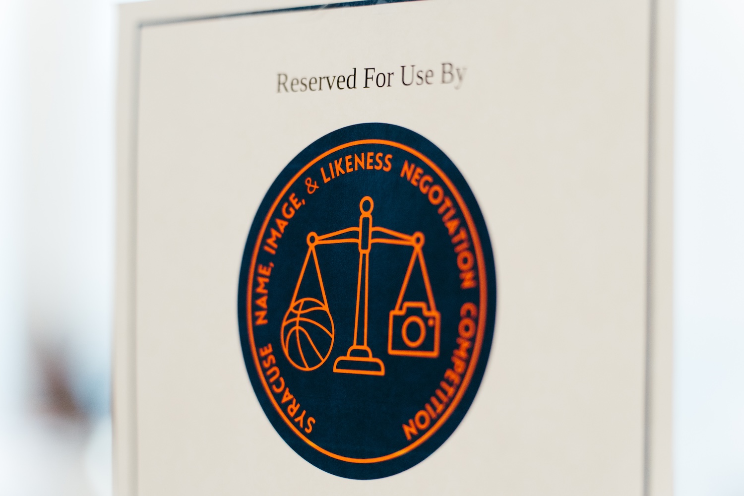 Logo for the Syracuse Name, Image & Likeness Negotiation Competition displayed on a sign.