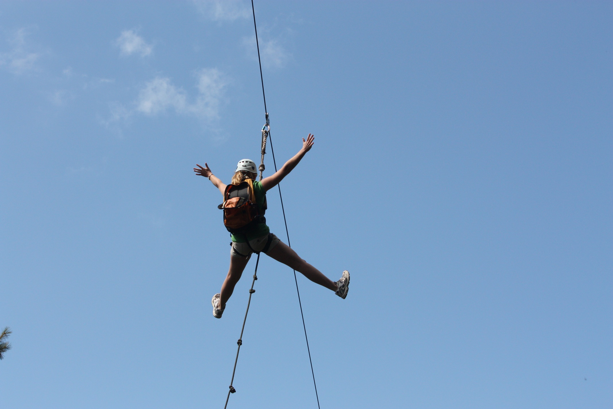 A person in a helmet and harness rides a zipline against a bright blue sky